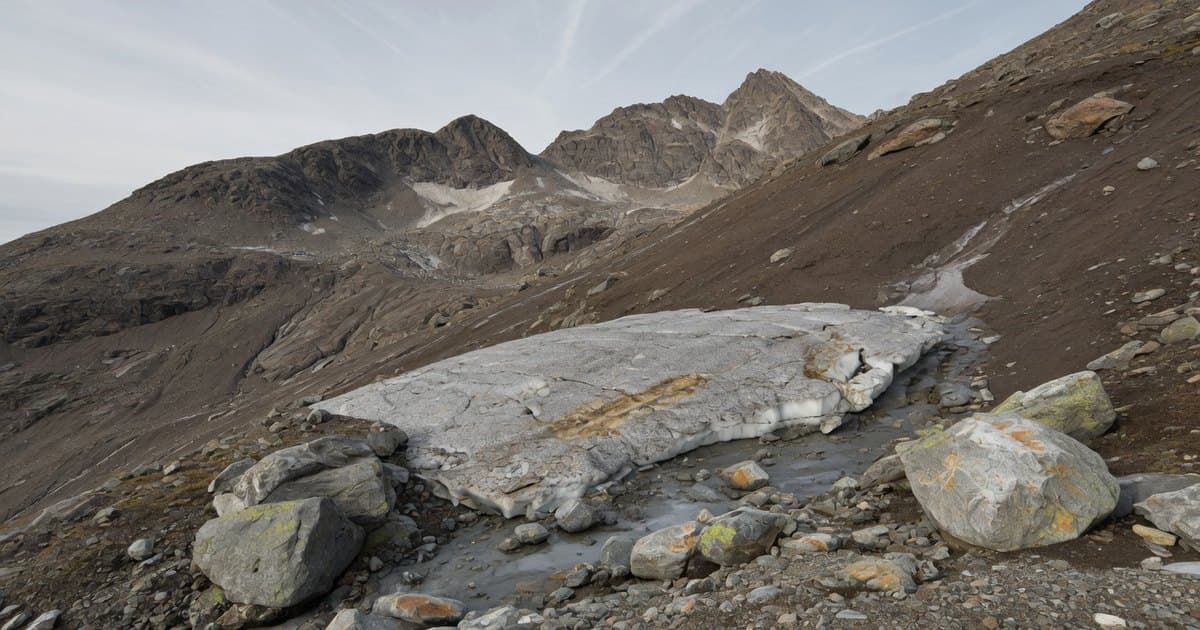 Pequeño remanente de hielo sucio sobre una ladera rocosa gris de alta montaña donde antes hubo un glaciar, con cumbres desnudas al fondo