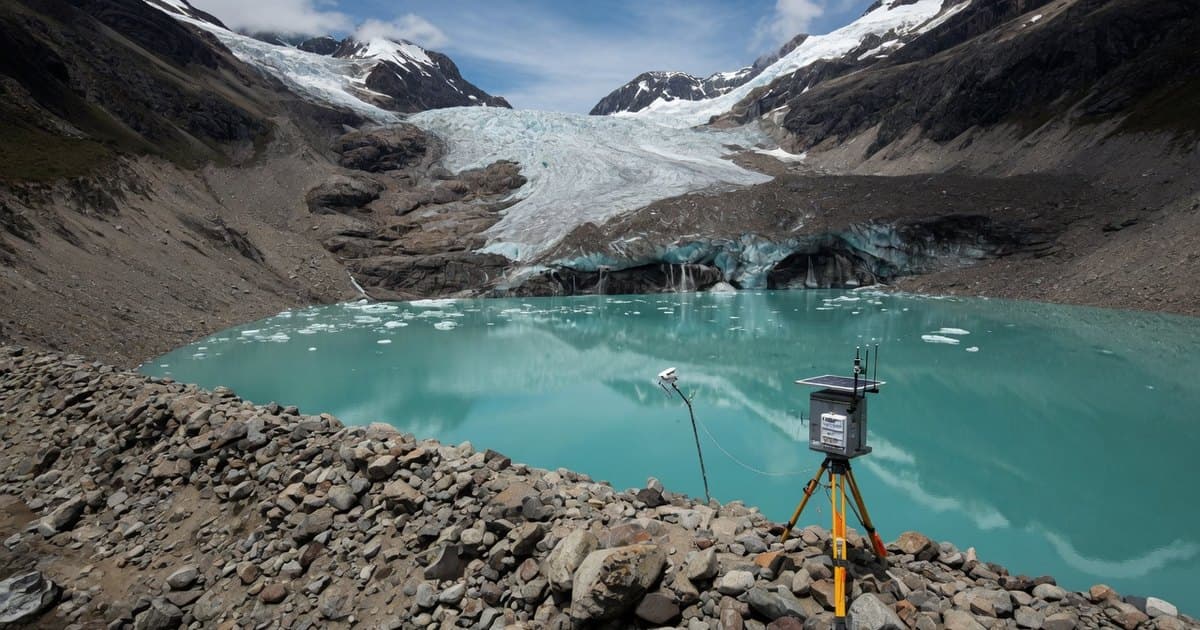 Laguna proglaciar turquesa al pie de un glaciar cubierto de detritos en los Andes, con una morrena en primer plano y un instrumento de medición sobre las rocas