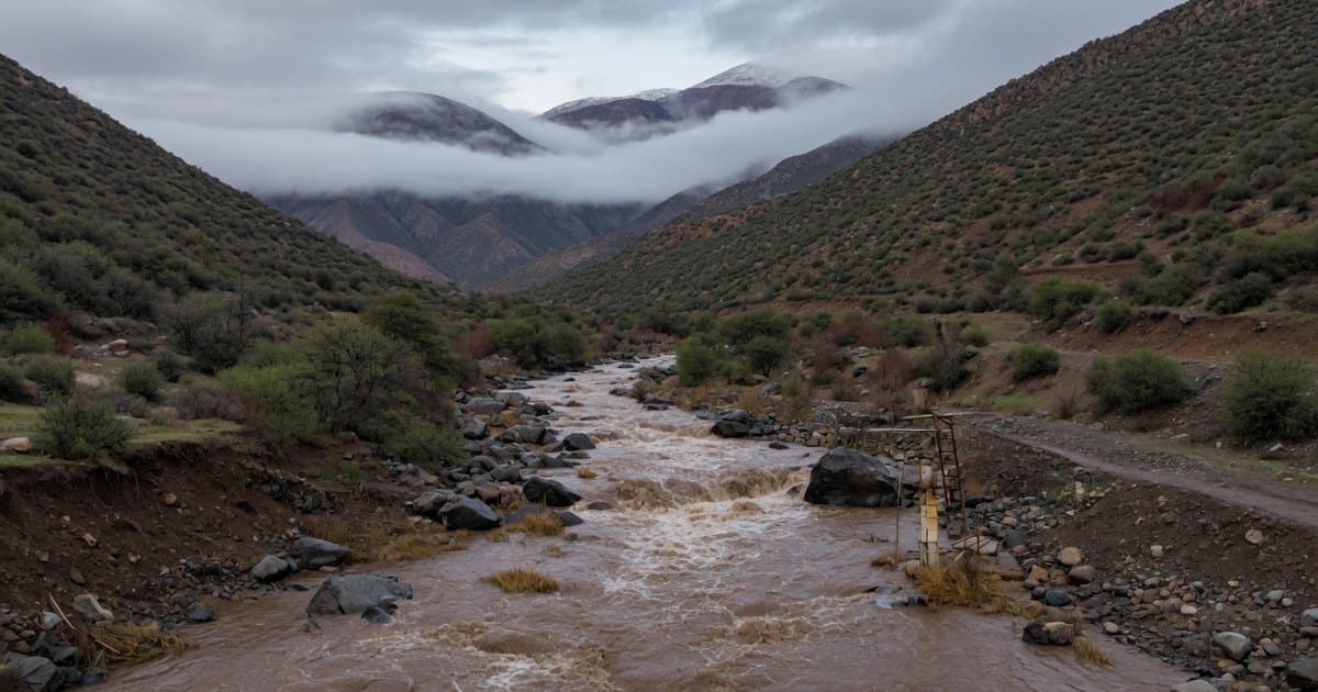 Quebrada precordillerana de Chile central con el cauce crecido y agua turbia bajando entre laderas con matorral